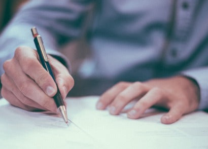 Mano firmando un documento legal con un bolígrafo en un escritorio